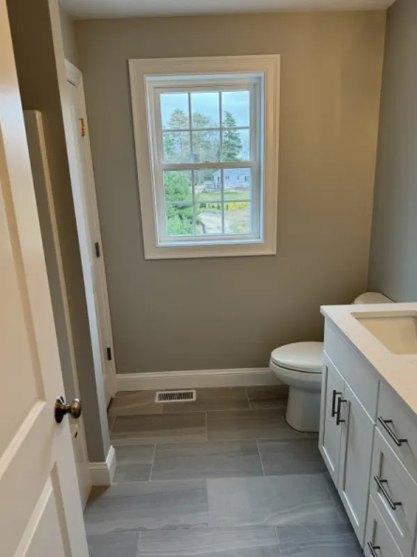 Small bathroom with a window, toilet, and white vanity under a neutral wall color.