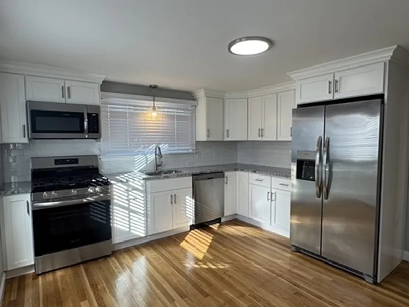 Modern kitchen with white cabinets, stainless steel appliances, and wooden floors.