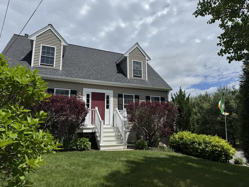 A two-story house with a red door, shrubs, and an Irish flag in the yard.