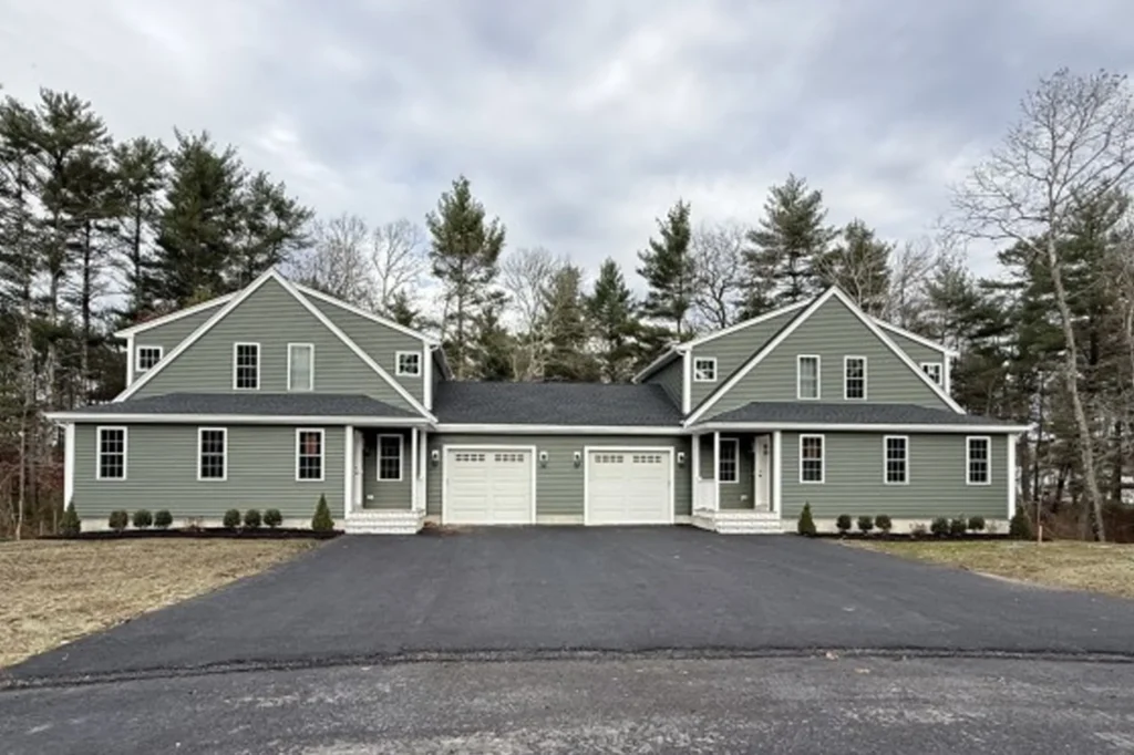 A green duplex house with two garages, white trim, and a wide paved driveway.