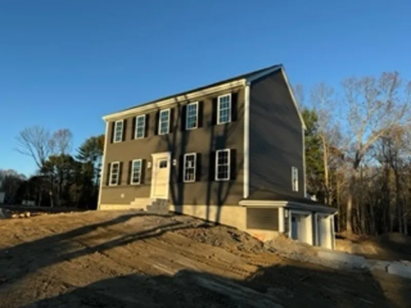 A two-story gray house with white trim, garage, and no landscaping, under a clear sky.