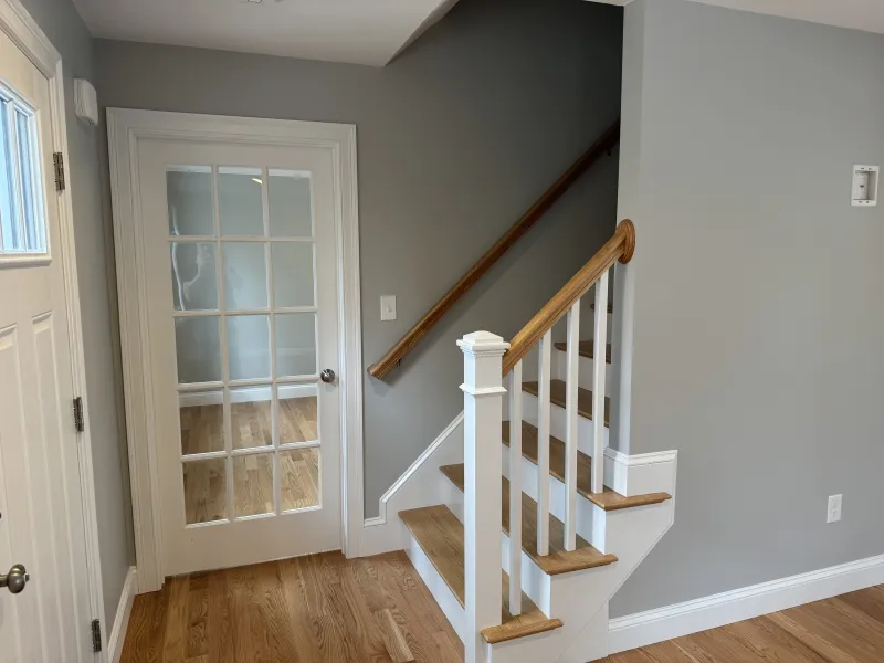 A small wooden staircase beside a glass-panel door in a hallway with gray walls.