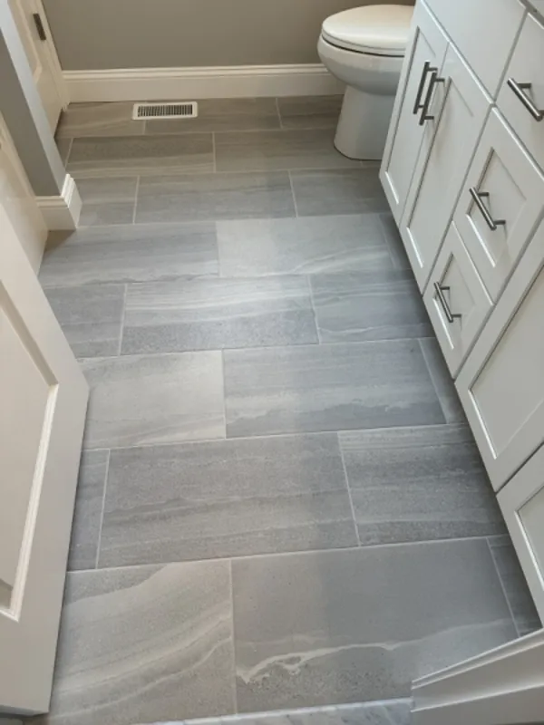 Gray rectangular bathroom tiles with white cabinetry and a toilet in the background.