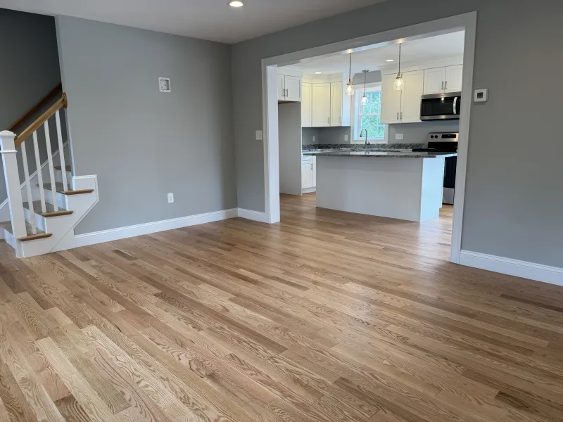 Open living area with wooden floors, gray walls, stairs, and view into a modern kitchen.
