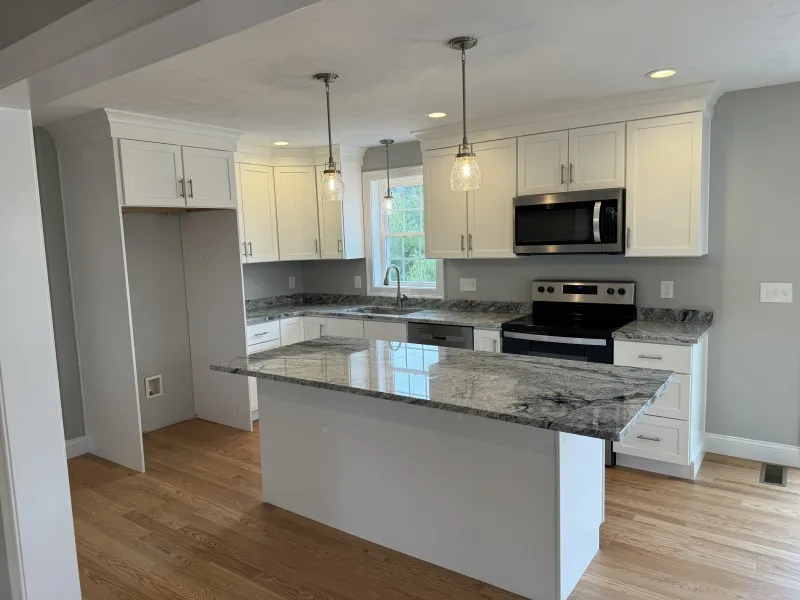 Modern kitchen with white cabinets, marble countertops, and stainless steel appliances.