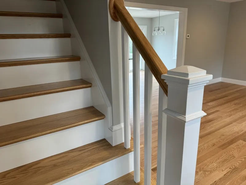 Wooden staircase with white trim and matching hardwood floor in a bright, modern home.
