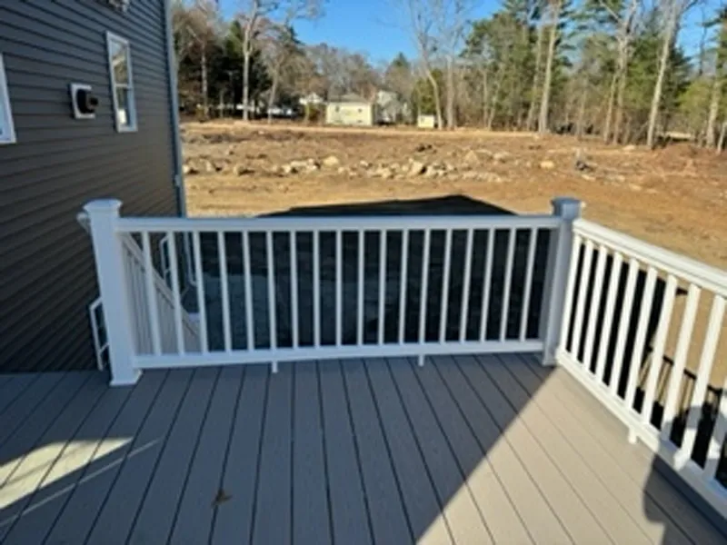 White-railed deck with gray floor overlooking a dirt yard and trees in the background.