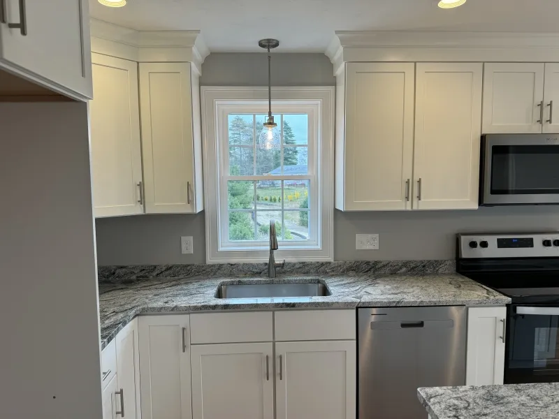 Kitchen with white cabinets, gray marble counters, and a window above the sink.