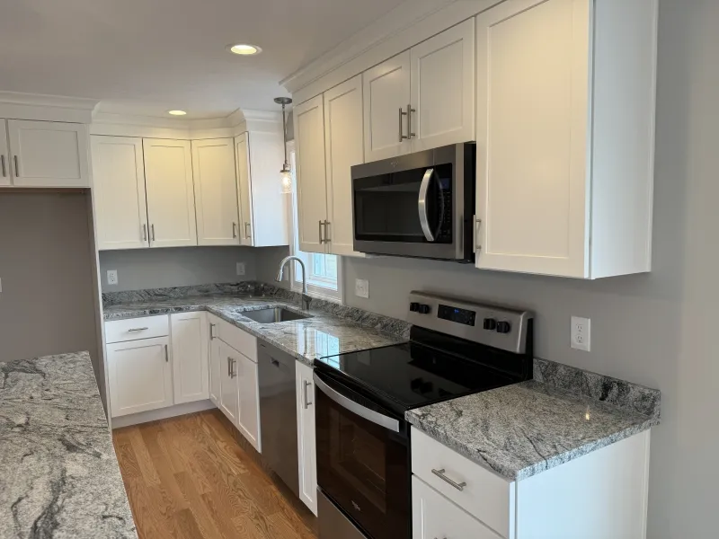 Modern kitchen with white cabinets, stainless appliances, and gray granite countertops.