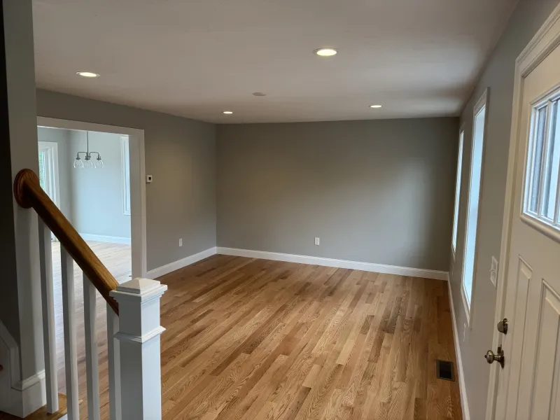 Empty living room with wood floors, gray walls, and recessed lighting by large windows.