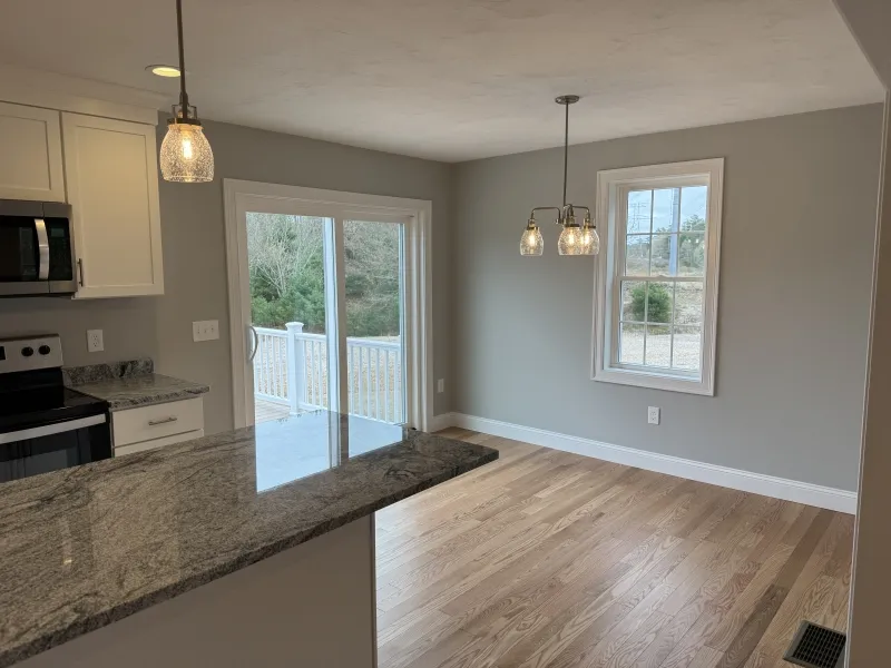 Bright kitchen and dining area with hardwood floors, pendant lights, and large windows.