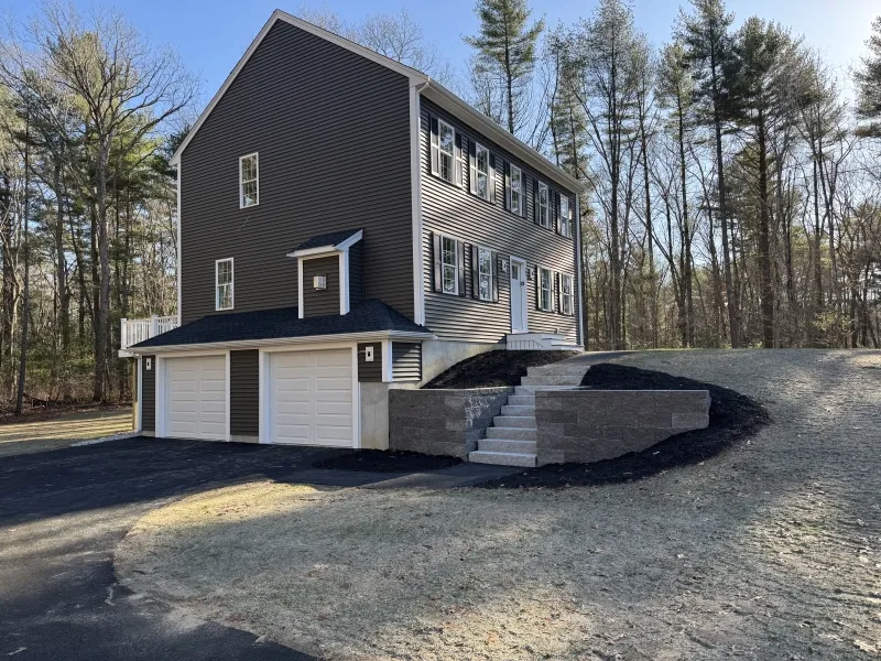 Three-story gray house with white trim, double garage, and a stone staircase in front yard.