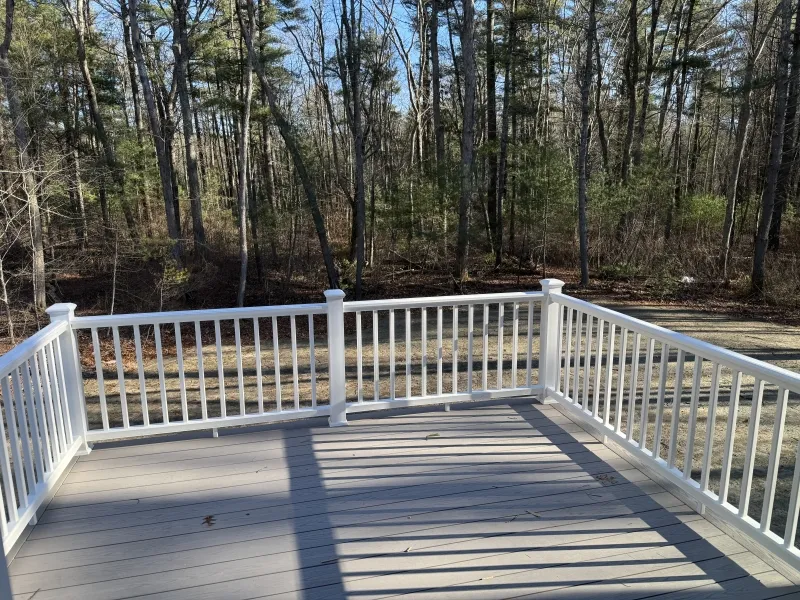 White-railed deck overlooking a wooded area with tall trees under a clear blue sky.