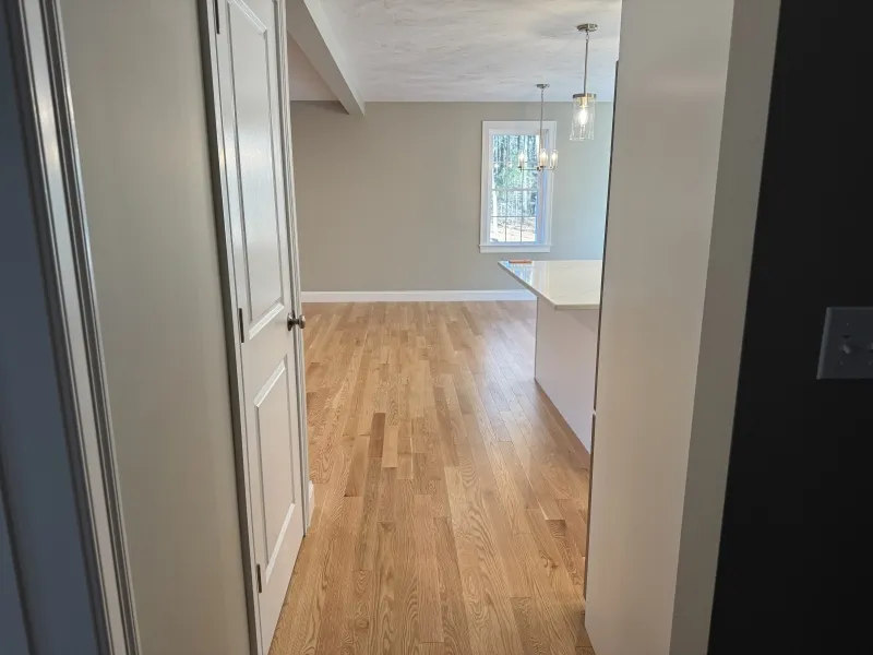 View of a room with light wood flooring, beige walls, and a window with sunlight.