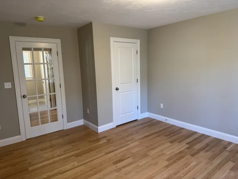 Empty room with hardwood floors, beige walls, a white door, and glass-paneled double doors.