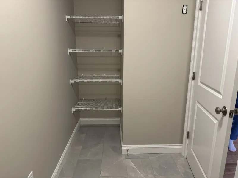 Empty closet with three white wire shelves, beige walls, and a tiled floor.