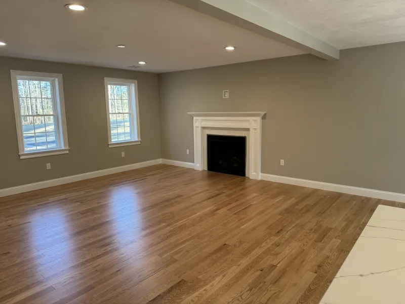 Spacious empty living room with hardwood floors, fireplace, and three windows.