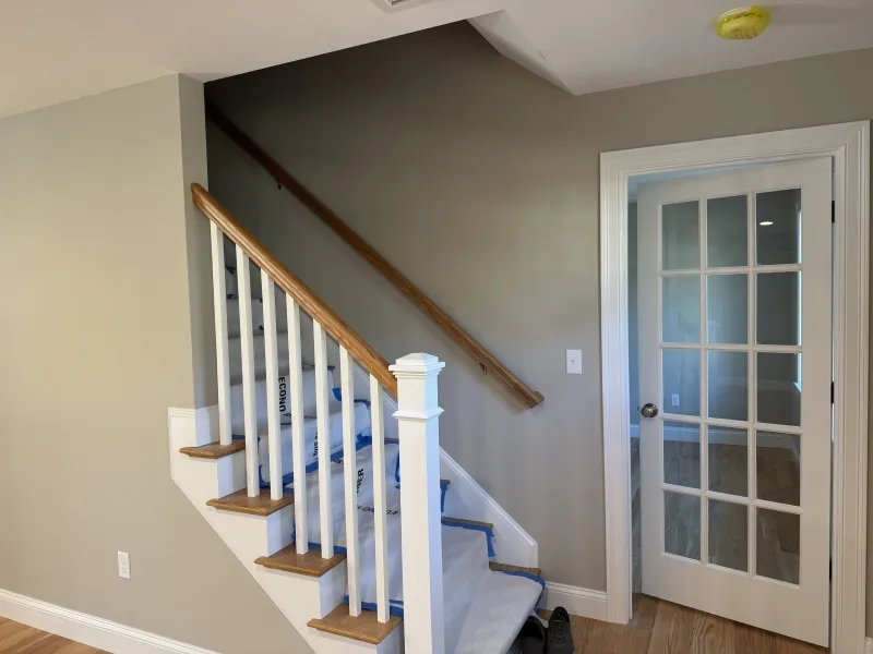 Wooden staircase with white railing next to a glass-paneled door in a beige hallway.