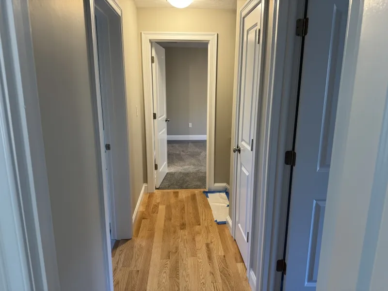 A hallway with wood flooring and several white doors leading to carpeted rooms.