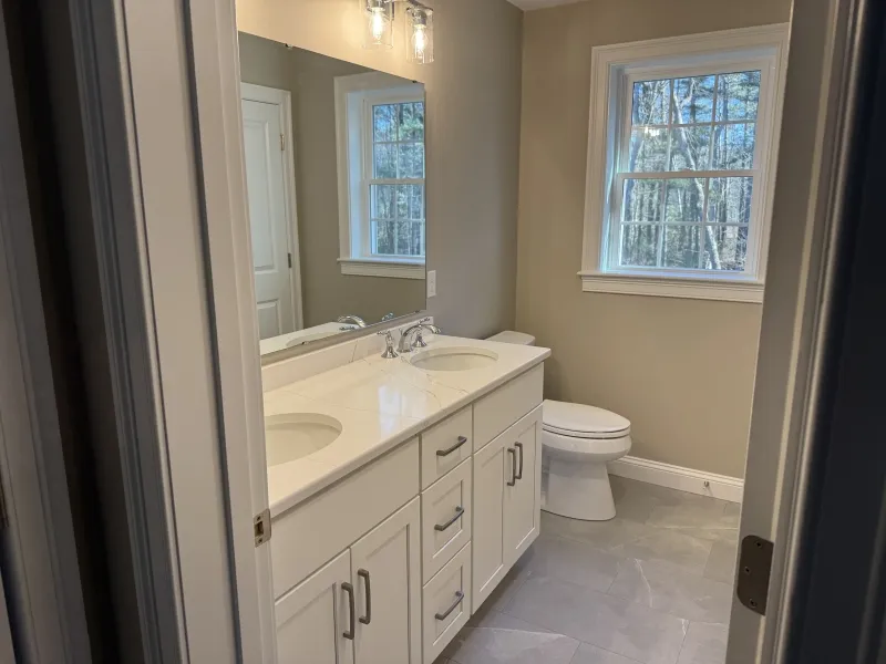 Modern bathroom with double sink vanity, large mirror, and window above a toilet.