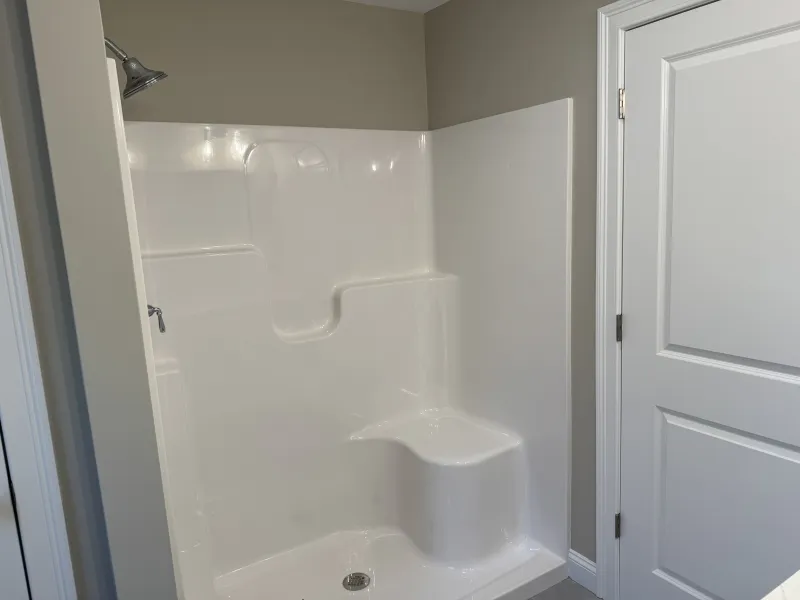 White walk-in shower with built-in seat, silver showerhead, and beige walls.
