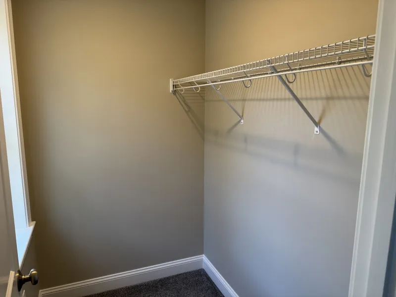 Empty walk-in closet with beige walls and a single white wire shelf on the right wall.