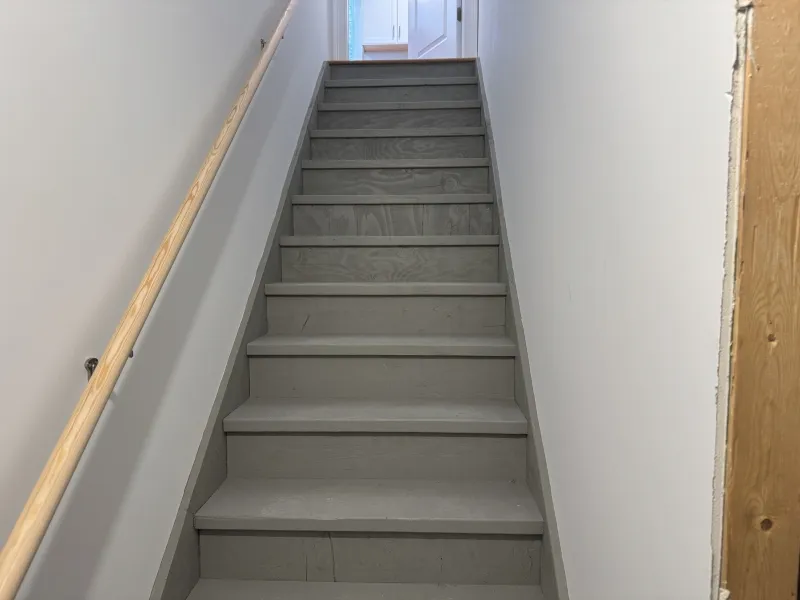 Gray indoor staircase with a wooden handrail, leading up to a white door at the top.