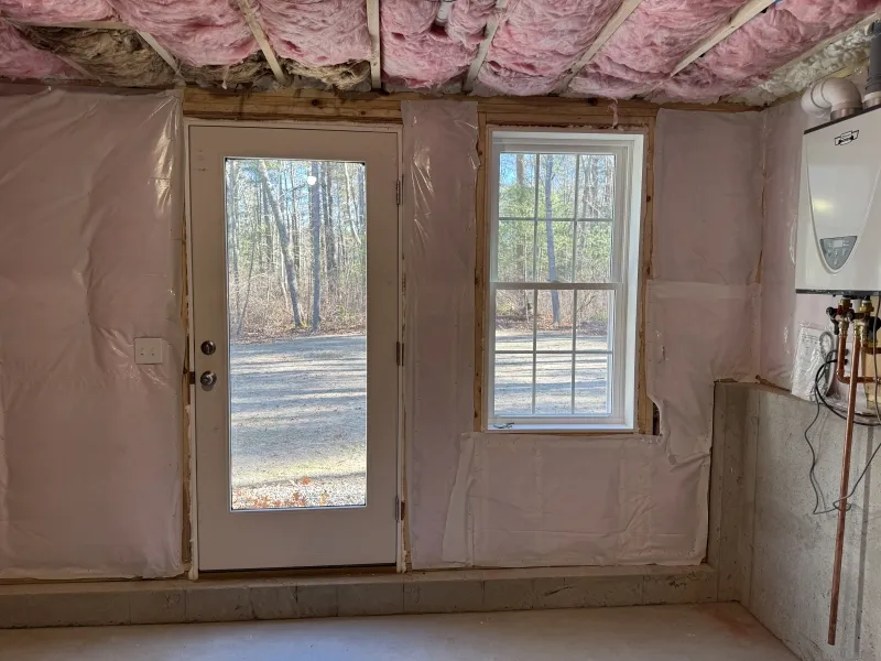 A room with unfinished walls and ceiling, showing insulation, a door, and a window.