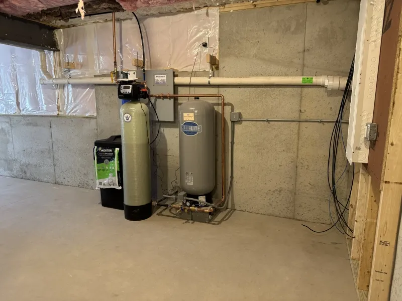 Water softener and pressure tank installed in an unfinished basement with concrete walls.