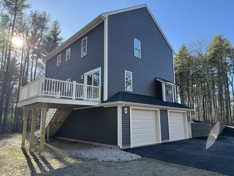 Tall gray house with white trim, two-car garage, and deck, surrounded by trees.