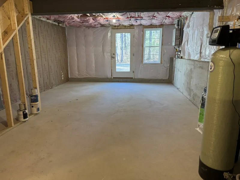 Unfinished basement with concrete floor, exposed framing, and a door leading outside.