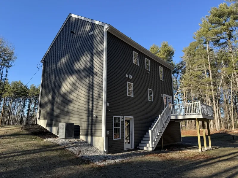 A dark gray house with side stairs and deck, surrounded by trees under a clear blue sky.