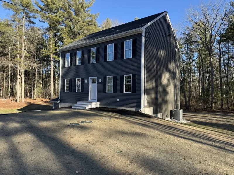 Two-story dark gray house with white trim, surrounded by trees on a sunny day.