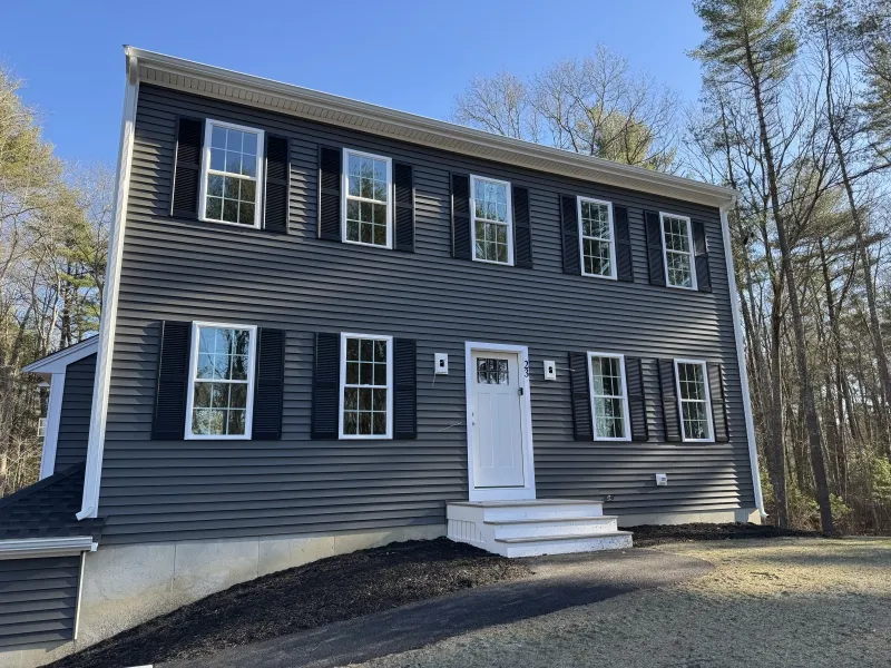 Two-story gray house with white trim, black shutters, and a front porch, near trees.