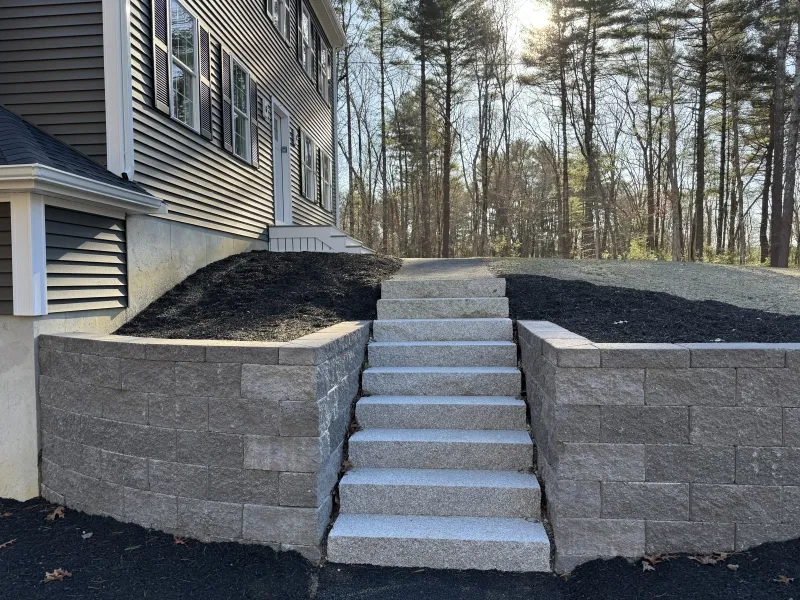 Stone steps with retaining walls lead up to a house with trees in the background.