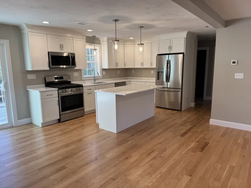 Modern kitchen with white cabinets, stainless appliances, island, and hardwood floors.