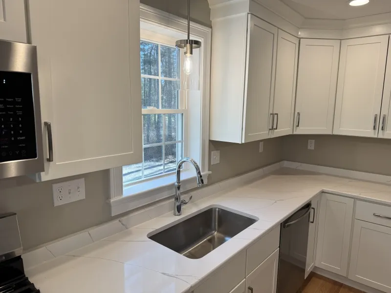 Modern kitchen with white cabinets, a stainless steel sink, and a large window above.