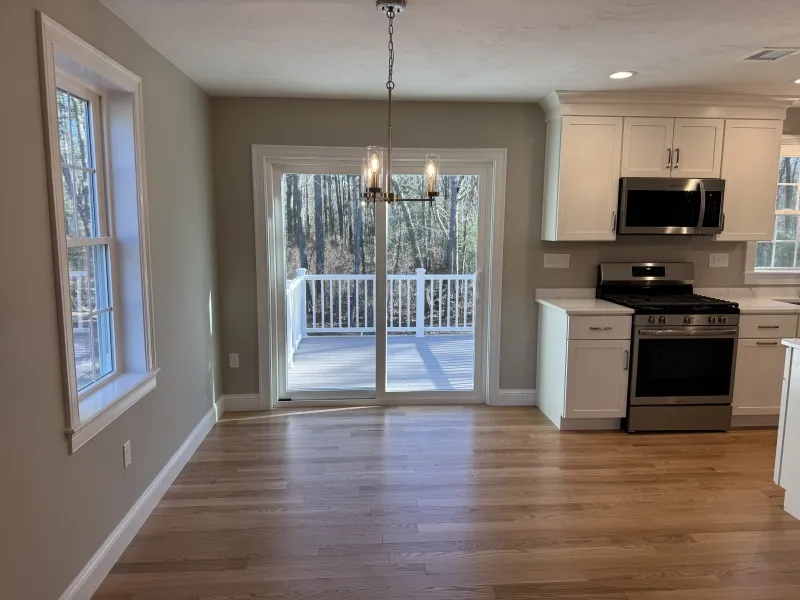 Kitchen with light wood floors, white cabinets, stove, and sliding doors to a deck.