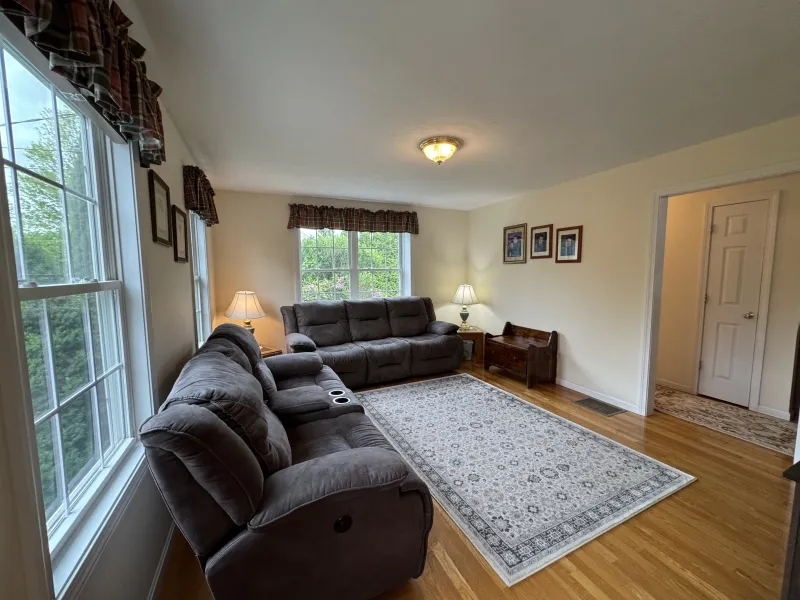 Living room with two gray sofas, large windows, lamps, framed photos, and a patterned rug.