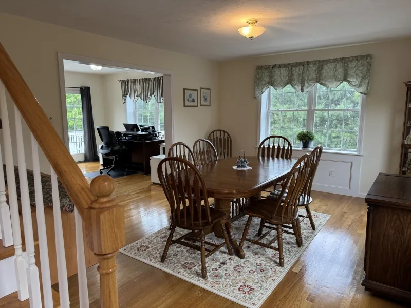 Dining room with wooden table, six chairs, and large window, next to a home office.