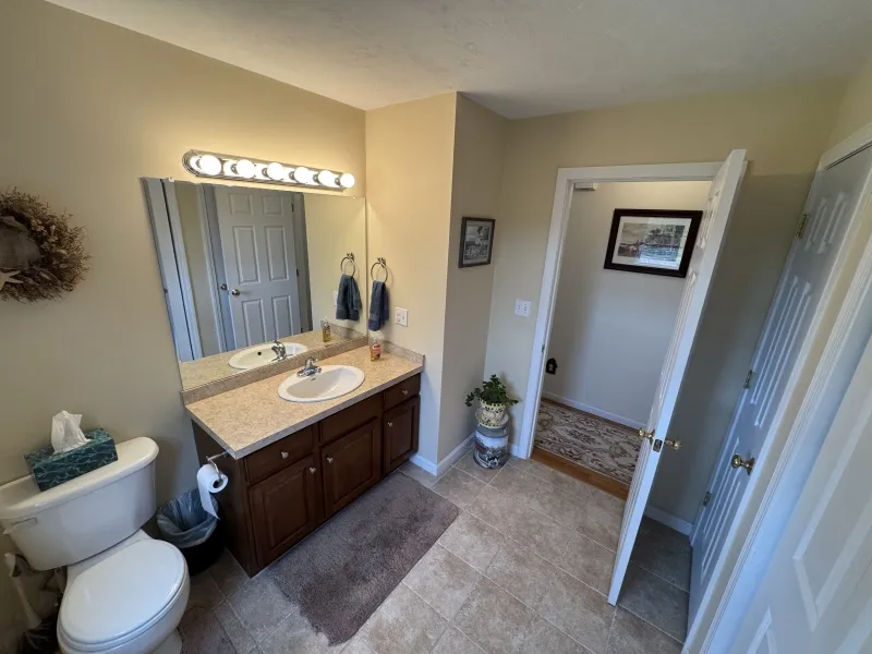 Bathroom with single sink, large mirror, toilet, and door open to a hallway.