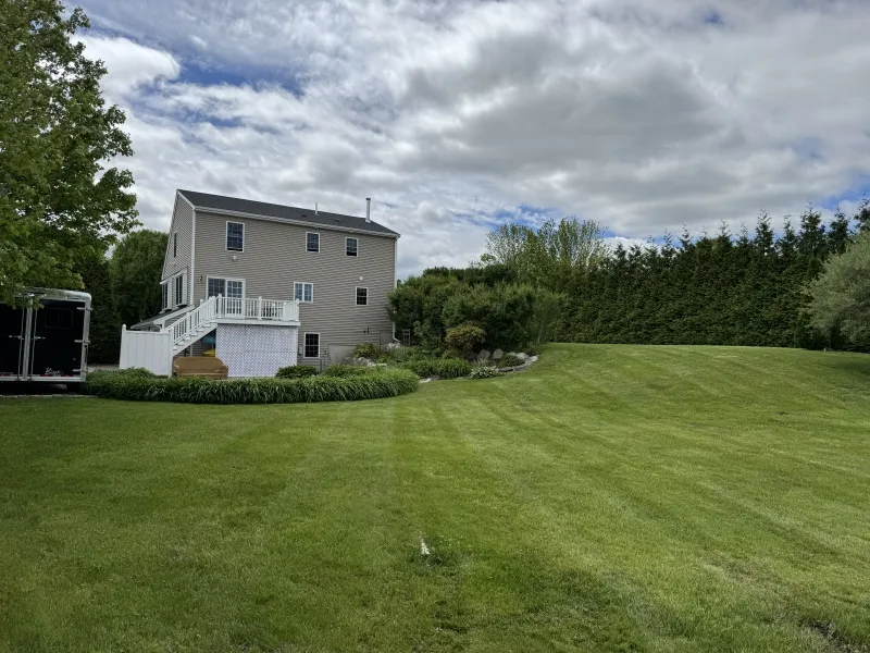 Two-story house with a deck overlooking a large, neatly mowed backyard and cloudy sky.