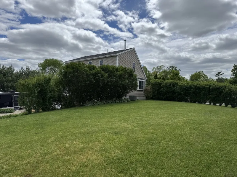 A house with hedge bushes and a large green lawn under a partly cloudy sky.